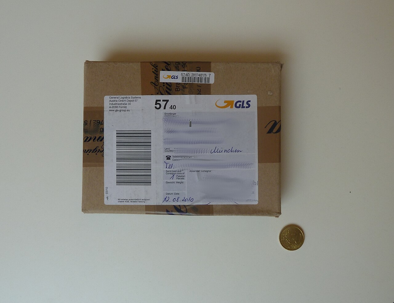 GLS shipping label on a small brown parcel, on a white table. Recipient information is masked in the published original.